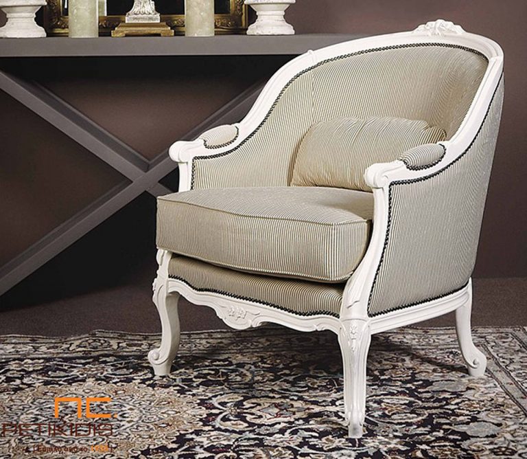 Πολυθρόνα Frida σε κλασική γραμμή με λεπτομέρειες ξύλου σε λευκή πατίνα. Το ύφασμα είναι σε εκρού αποχρώσεις με λεπτή ρίγα και διαθέτει διακοσμητικό μεταλλικό καμπαρά.